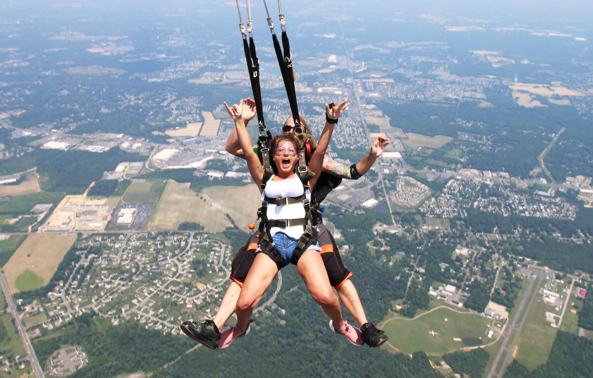 Girl raises arms as she glides on tandem parachute ride.