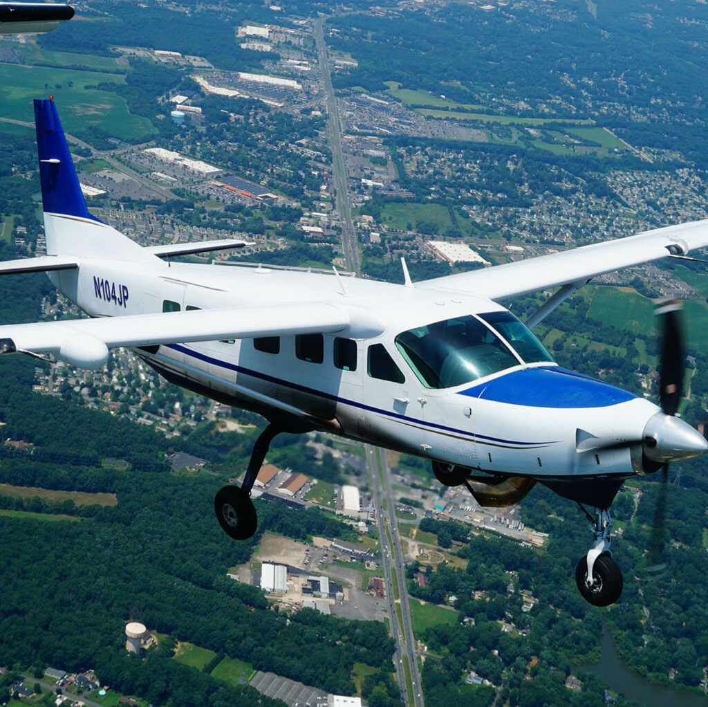 Cessna Caravan plane in mid-flight from above with a green landscape far below.