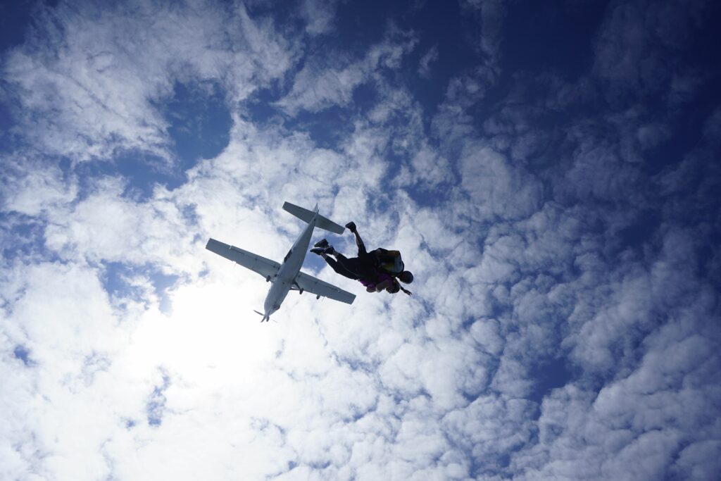 View from below of tandem skydivers just after they jump out of the plane with the clouds and blue skies above.