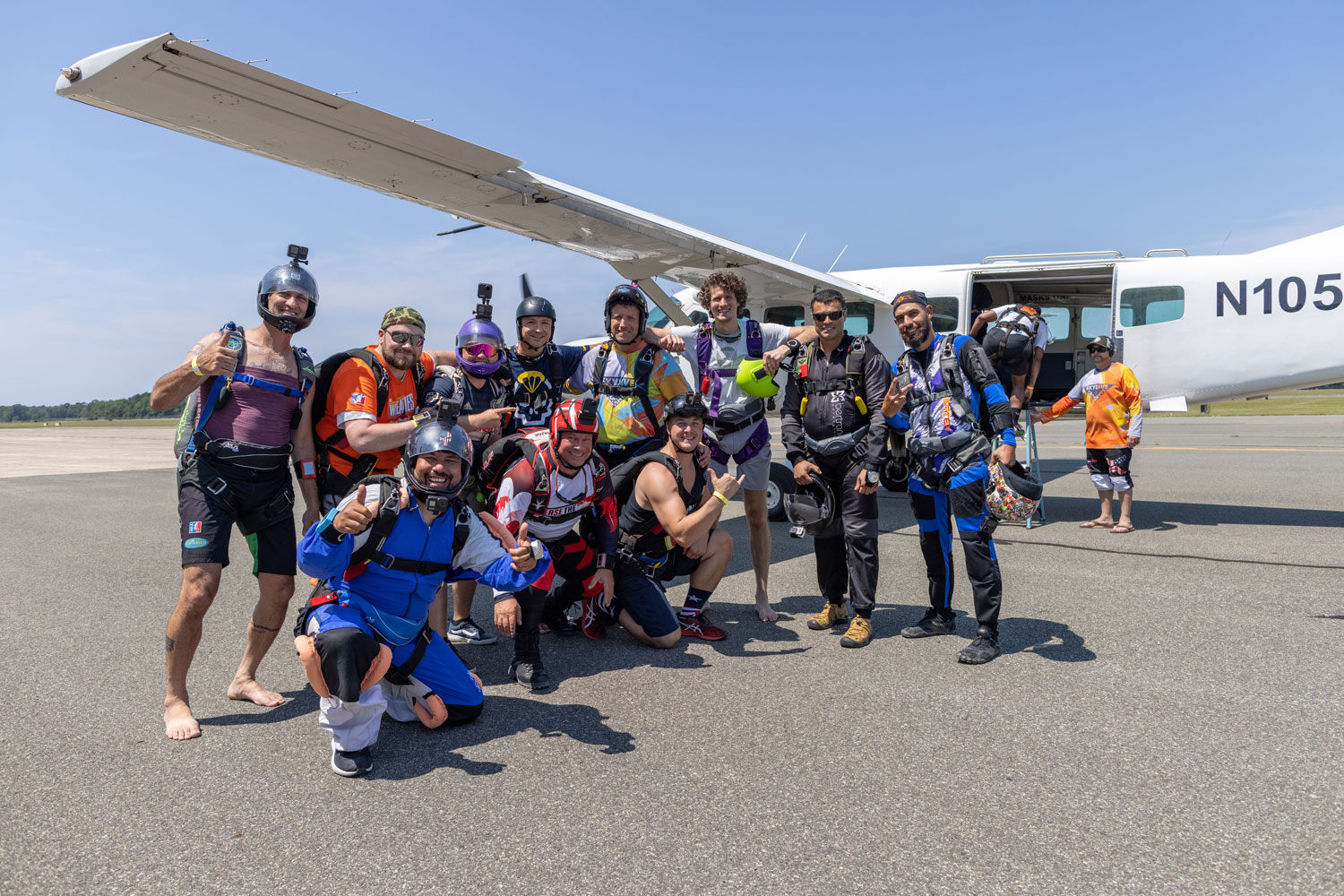 Group of skydivers smiling and posing in front of the plane.