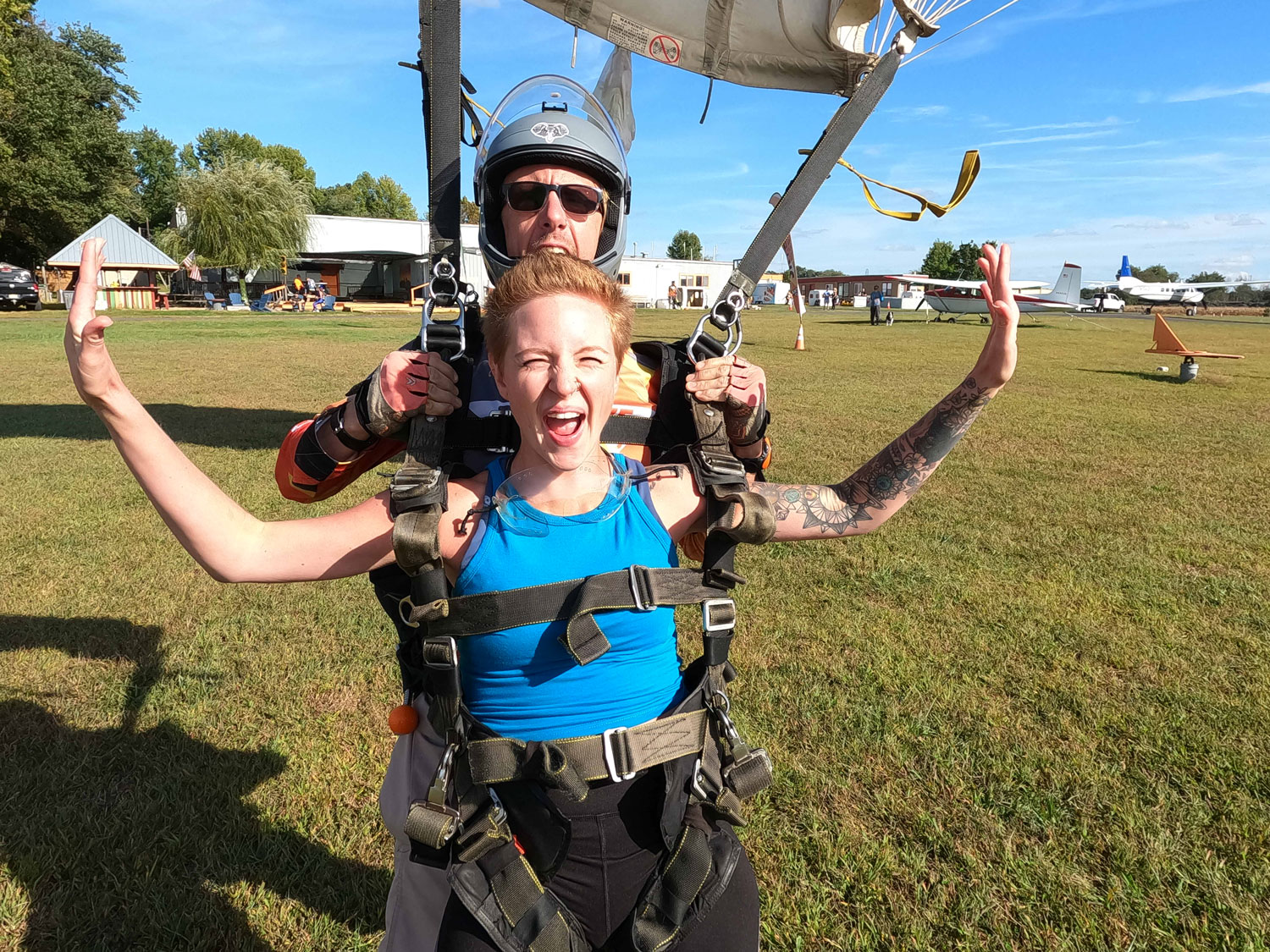 Smiling tandem skydivers after landing in a field by parachute.