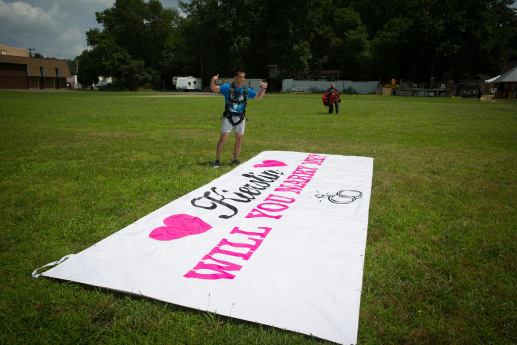 Will you marry me banner on ground with skydiver.