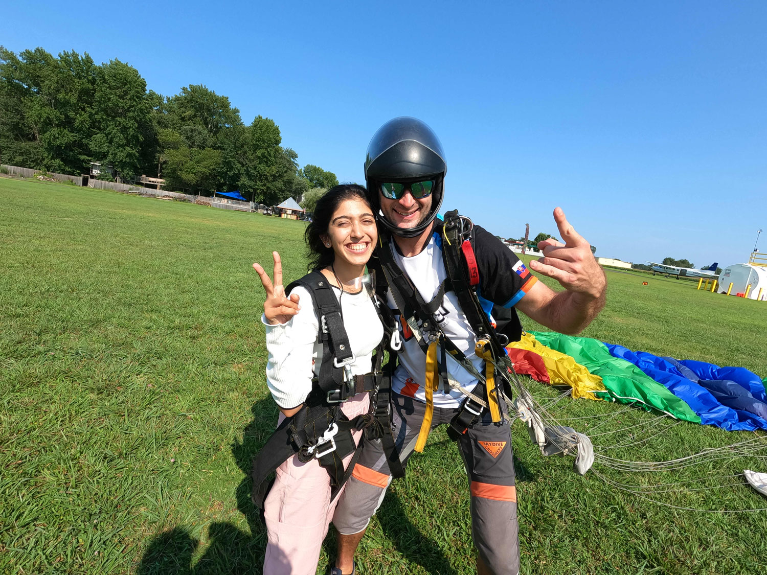 Tandem skydiver with instructor after landing with parachute lying in the grass in the background.