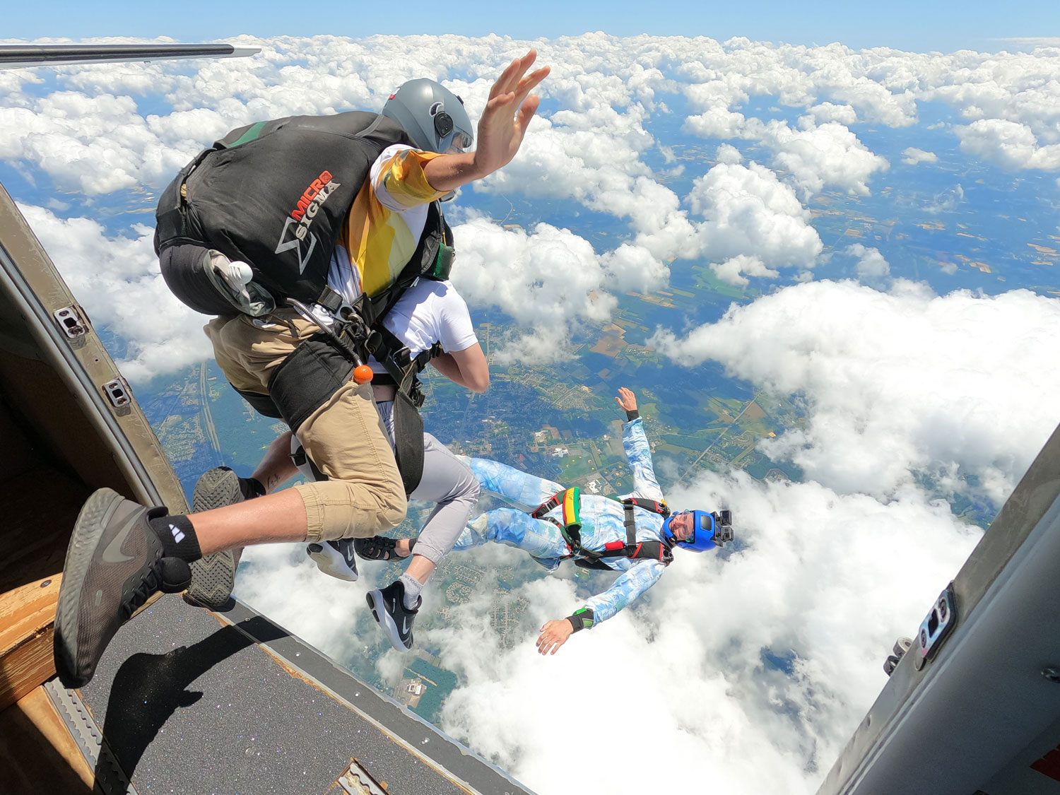 Tandem skydivers just after jumping from the plane shown from above with clouds below.